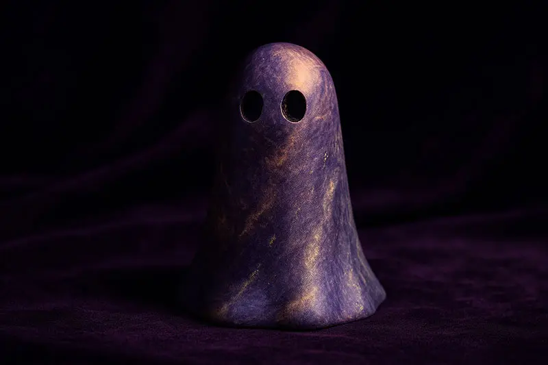 A marbled ghost figurine in violet, indigo, pale gold, and grey glowing softly against a twilight backdrop.